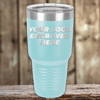 A light blue Kodiak Coolers tumbler with a stainless steel lid rests on wood, featuring "YOUR LOGO ENGRAVED HERE." This Engraved Custom Logo Drinkware includes single-side engraving and bulk pricing—ideal for branded mugs.