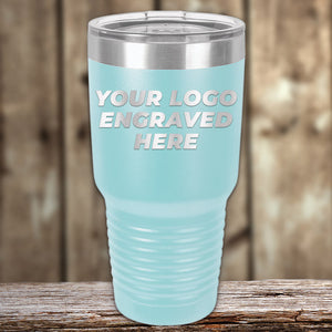 A light blue Kodiak Coolers tumbler with a stainless steel lid rests on wood, featuring "YOUR LOGO ENGRAVED HERE." This Engraved Custom Logo Drinkware includes single-side engraving and bulk pricing—ideal for branded mugs.