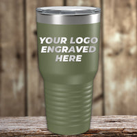A green Kodiak Coolers stainless steel tumbler with a clear lid sits on wood, featuring "YOUR LOGO ENGRAVED HERE." This Engraved Custom Logo Drinkware includes single side engraving and bulk tiered pricing—ideal for personalized gifts.
