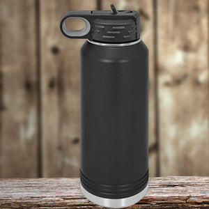 A black insulated stainless steel water bottle with a loop handle lid, resting on a wooden surface against a blurred wooden background. - Custom Water Bottles 32 oz with your Logo or Design Engraved by Kodiak Coolers