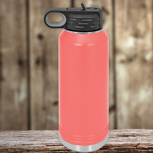 A coral red Kodiak Coolers insulated stainless steel water bottle with a black flip-top lid, positioned on a wooden surface against a blurred wooden backdrop.