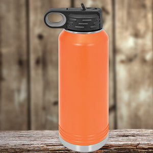 Orange Kodiak Coolers insulated stainless steel water bottle with a black cap, placed on a wooden surface against a blurred wooden backdrop.