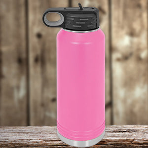 Pink Kodiak Coolers insulated stainless steel water bottle with a black flip-top lid, resting on a wooden surface against a blurred wooden backdrop.