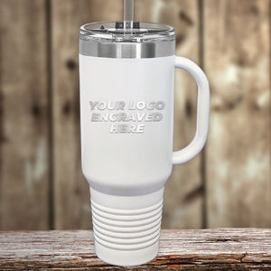 A Kodiak Coolers custom engraved white travel mug with a handle and straw lid sits on a wooden surface. The tumbler reads, "YOUR LOGO ENGRAVED HERE." Perfect for those seeking wholesale pricing, it requires a $250 minimal order during the Presidents Day Sale.