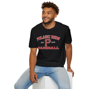 A man in light blue jeans sits on a white block, smiling to the side while wearing the Printify "P Reds Baseball Est. 1978 - Unisex Softstyle T-Shirt Volume.
