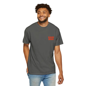 A man wearing a dark gray BODE Summer Camp T-Shirt 2026 "Throwback Sunset" by Printify and light blue jeans stands against a white background, smiling with one hand in his pocket.