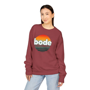 A woman stands against a white background wearing the Printify 2026 Bode Summer Bootcamp Crewneck Sweatshirt GDH400, a maroon, garment-dyed Hanes Comfortwash midweight fleece featuring a "bode summer camp" sunset graphic.