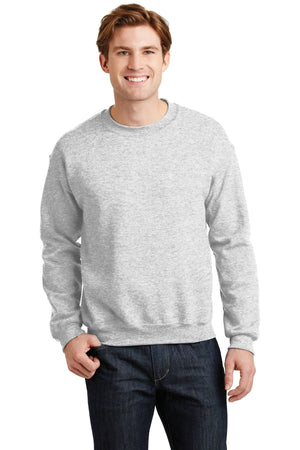 A person stands smiling against a plain white background, wearing a light grey Gildan Heavy Blend Crewneck Sweatshirt 18000 and dark jeans.