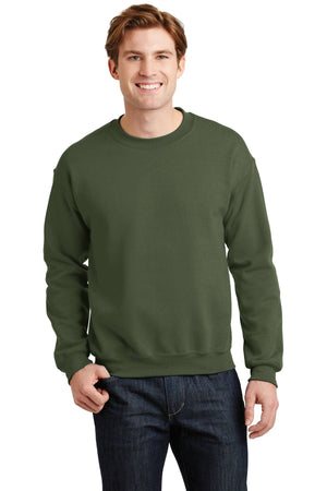 A person wearing a Gildan Heavy Blend Crewneck Sweatshirt 18000 in green and dark jeans stands smiling against a plain background.