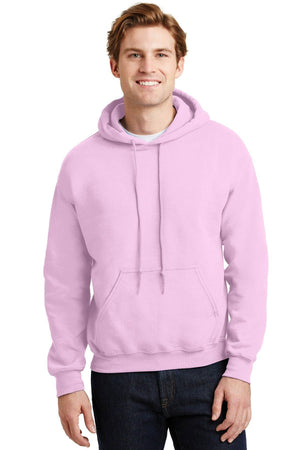 A man wears a light pink Gildan Heavy Blend™ Hooded Sweatshirt 18500 (Pack of 36) with custom screen printed logo, made sustainably, and dark jeans as he stands facing forward and smiles at the camera.