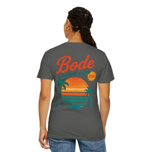 Wearing the BODE Summer Camp T-Shirt 2026 — "Throwback Sunset" by Printify (Comfort Colors 1717), featuring a retro sunset, ocean, and palm tree graphic in gray on the back. Unisex relaxed fit.