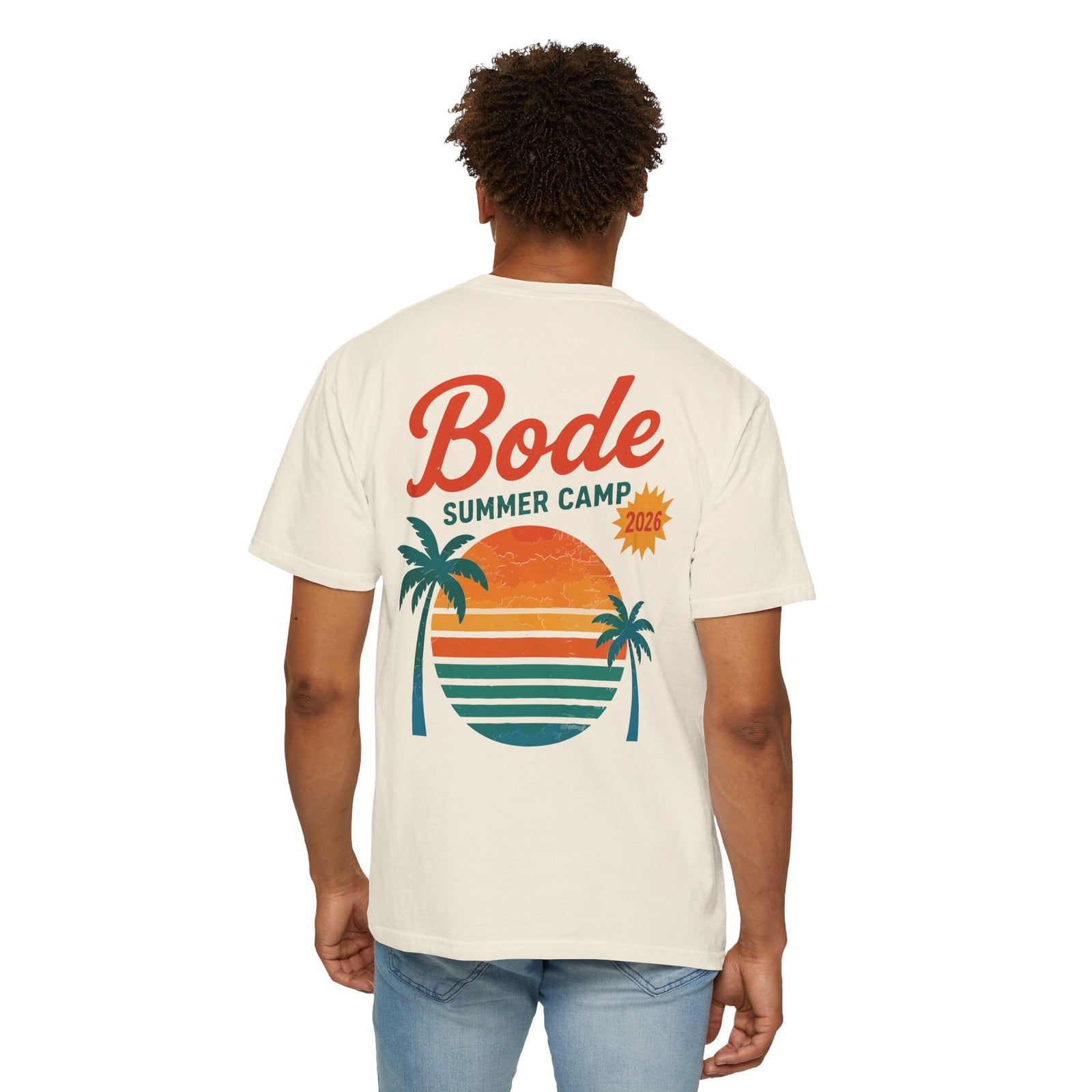 A person wearing a Printify BODE Summer Camp T-Shirt 2026—"Throwback Sunset," a unisex Comfort Colors 1717 heavyweight cotton shirt featuring sunset, palm trees, and ocean graphics on the back.