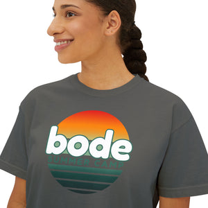 Smiling woman in a relaxed, boxy cropped Printify 2026 Bode Summer Bootcamp Cali Sunset Logo T-Shirt, featuring "bode summer camp" text and sunset graphic on soft ring-spun cotton.