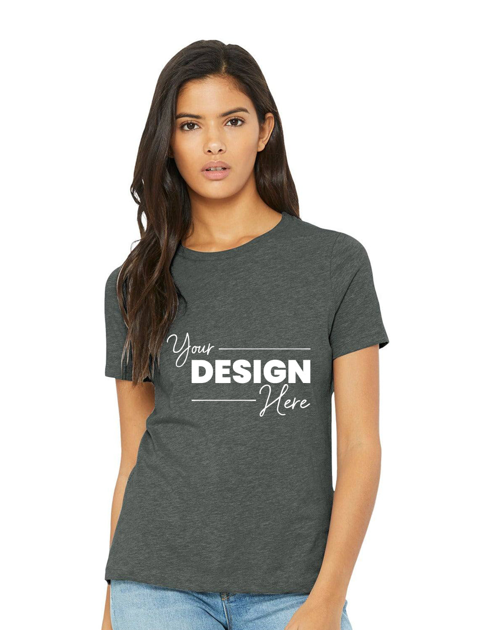 A person is wearing a relaxed-fit dark gray Bella + Canvas Women's CVC T-Shirt BC6400CVC with "Your Design Here," paired with blue jeans and standing against a plain white background.