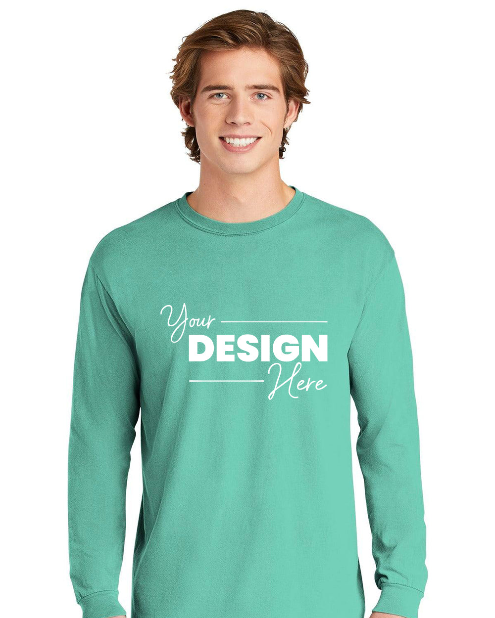 A smiling person wears a Comfort Colors Heavyweight Ring Spun Long Sleeve T-Shirt 6014 in mint green, featuring “Your Design Here” printed in white on the front.