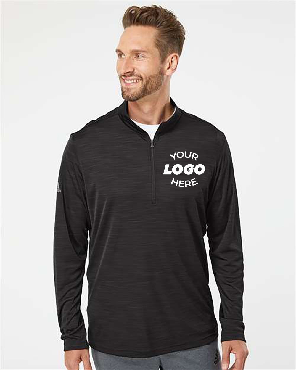 A man is wearing an Adidas Lightweight Melange Quarter-Zip Pullover in black, featuring the text "Your Logo Here" printed on the chest. This pullover, crafted from lightweight fabric, provides UPF 50+ protection. He is looking to the side and smiling.
