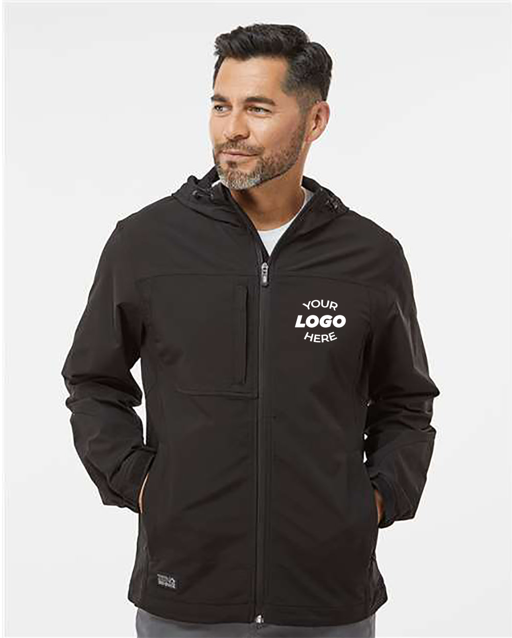 A man with short dark hair and a beard is wearing a black DRI DUCK Apex Soft Shell Hooded Jacket, which is wind-and-water resistant and has "Your Logo Here" displayed on the left side of the chest. He is looking to his left with a neutral expression.