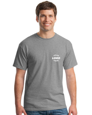 A man in a Gildan Heavy 100% Cotton Custom T-Shirt (Pack of 36), featuring a white "Your Logo Here" screen-printed on the left chest, stands and smiles.