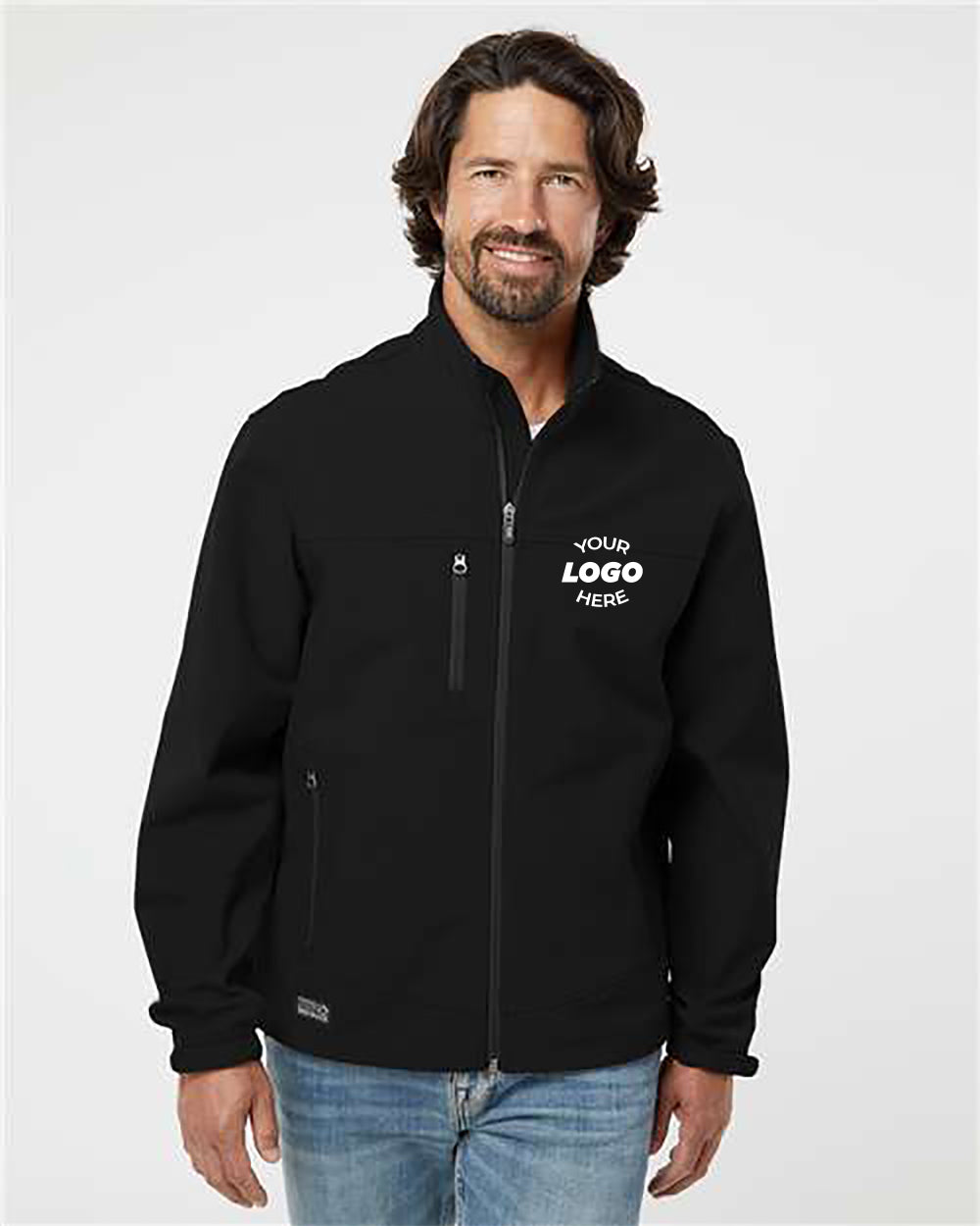 A man with wavy hair and a beard is wearing a black DRI DUCK Motion Soft Shell Jacket, which is wind-and-water-resistant and features "Your Logo Here" printed on the left chest. Standing against a plain white background, he showcases this customized jacket, ideal for businesses looking for wholesale pricing options.