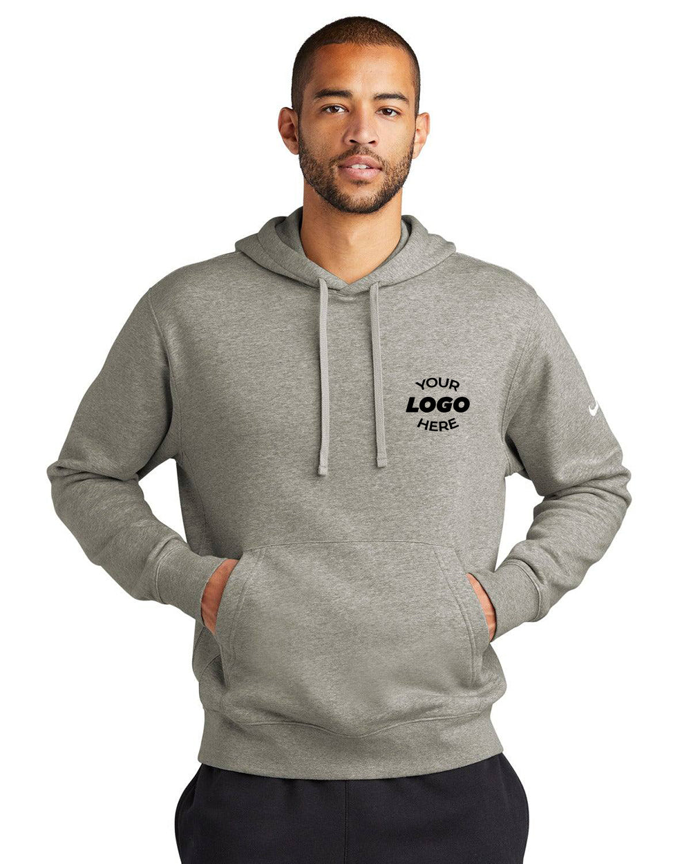 A man wearing a gray Nike Club Fleece Sleeve Swoosh Pullover Hoodie Sweatshirt NKDR1499, with "Your Logo Here" printed on it, has his hands in the front pocket, showcasing a casual, street-ready look against a white background.
