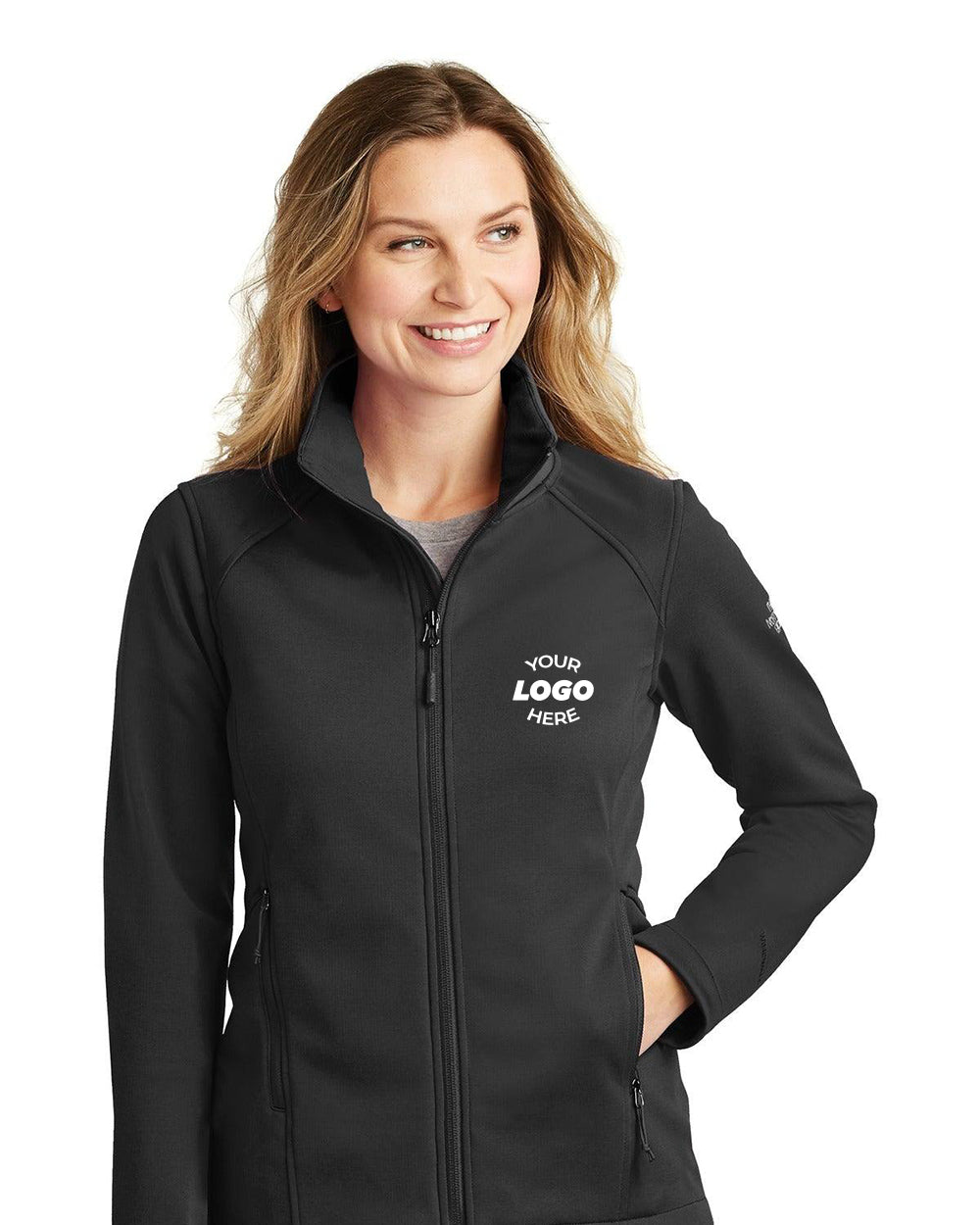 A person wearing The North Face Ladies Ridgewall Soft Shell Jacket NF0A3LGY with "YOUR LOGO HERE" on the chest, made from WindWall fabric for warmth, smiles while looking to the side.