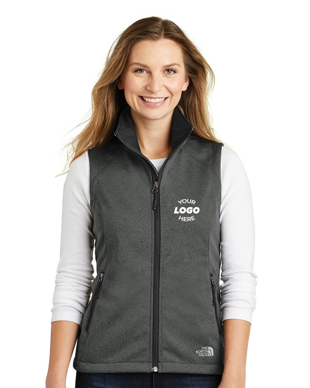 A woman wears a dark gray The North Face Ladies Ridgewall Soft Shell Vest (NF0A3LH1) over a white long-sleeve shirt, with "Your Logo Here" on the wind-resistant left chest.