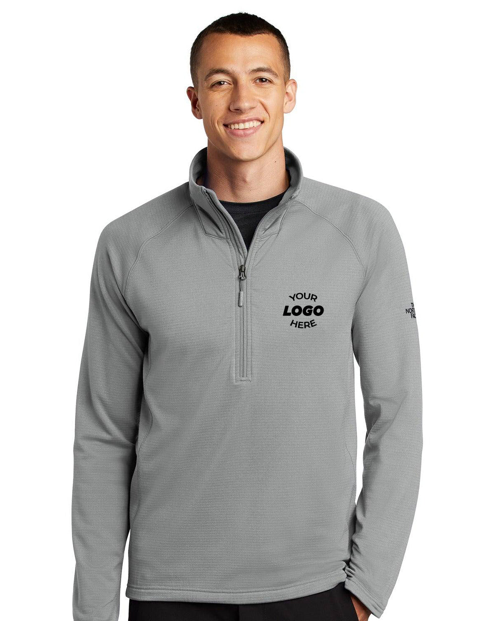 A man wears a light gray The North Face Mountain Peaks 1/4-Zip Fleece Pullover (NF0A47FB) with "Your Logo Here" on the left chest and a small logo on the left sleeve, ideal for standout corporate outerwear.
