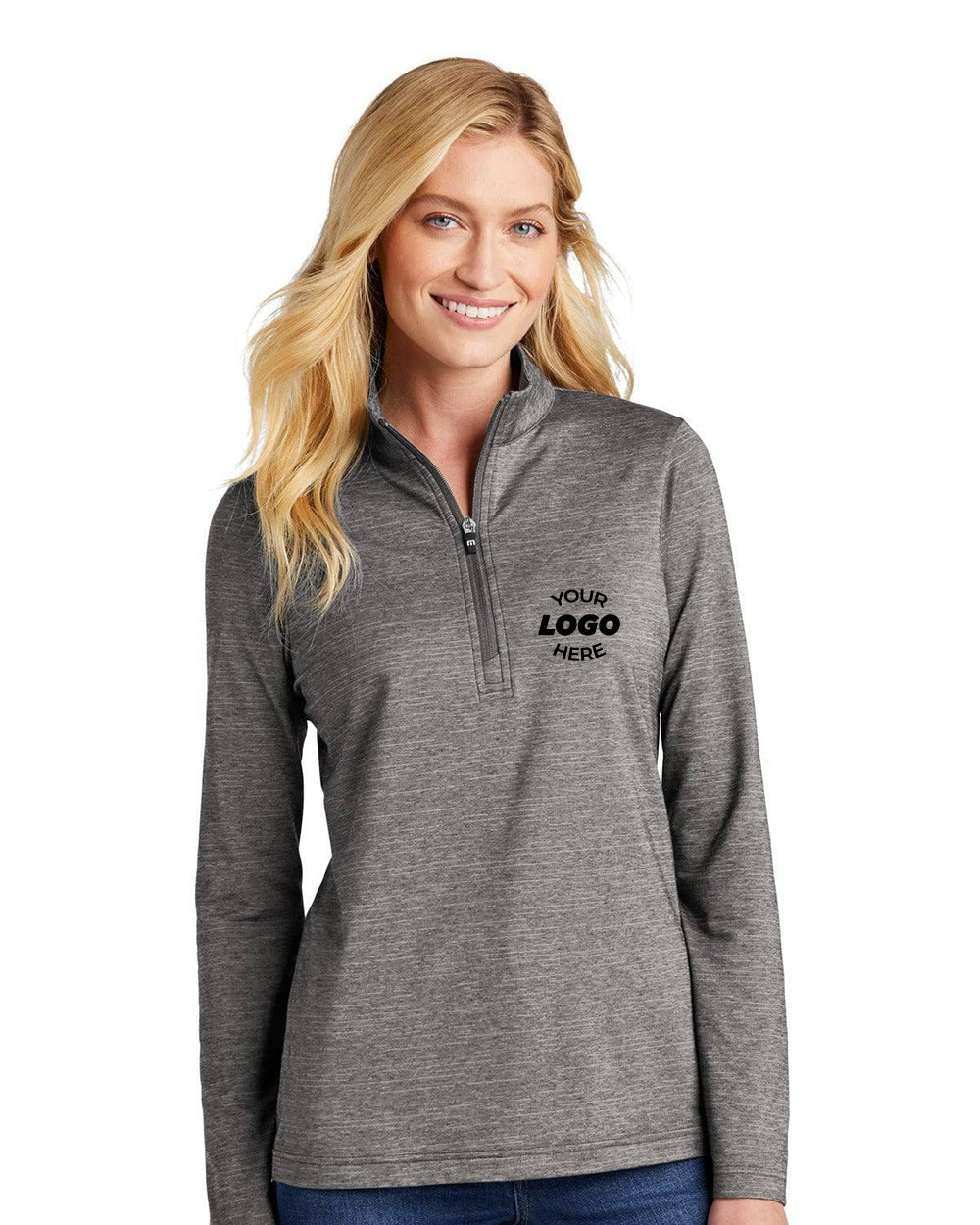 A woman stands against a white background wearing the TravisMathew Ladies Crestview 1/4-Zip Pullover (TM1WW003), a feminine-fit, lightweight gray long-sleeve with "Your Logo Here" printed on the left chest.