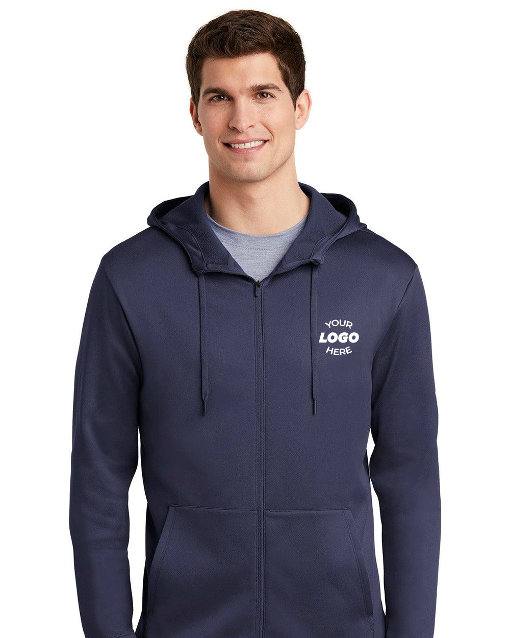 A person is smiling with hands in pockets while wearing a navy Nike Therma-FIT Full-Zip Fleece Hoodie Sweatshirt NKAH6259 featuring the "YOUR LOGO HERE" text on the front.