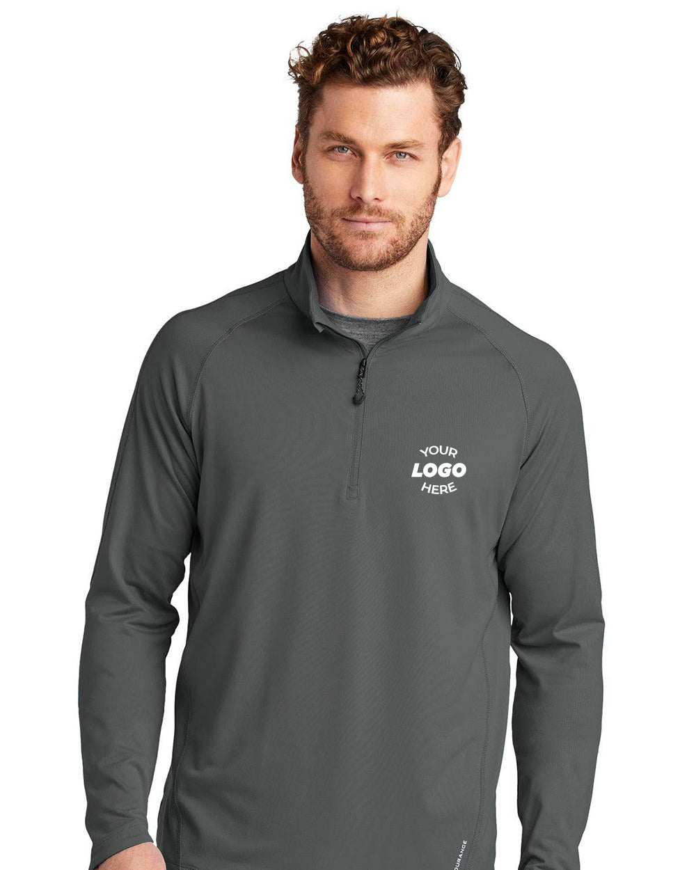A man with short curly hair wears a dark gray OGIO ENDURANCE Radius 1/4-Zip Pullover OE550, featuring "Your Logo Here" in reflective heat transfer on the left chest and stay-cool wicking technology for all-day comfort.