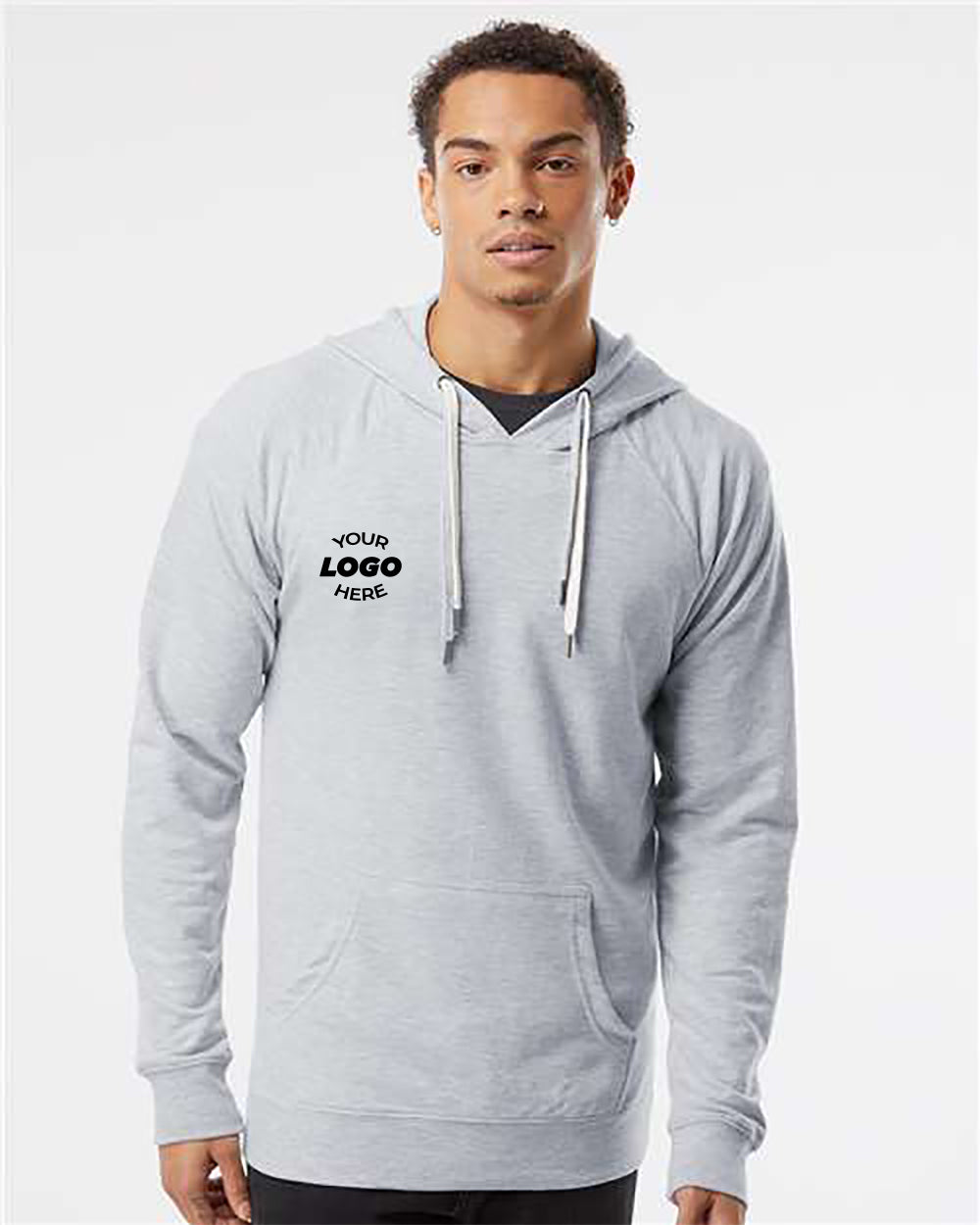 A person wearing an Independent Trading Co. Icon Unisex Lightweight Loopback Terry Hoodie Sweatshirt in light gray, featuring white drawstrings and a "Your Logo Here" design on the left chest, is standing against a white background.