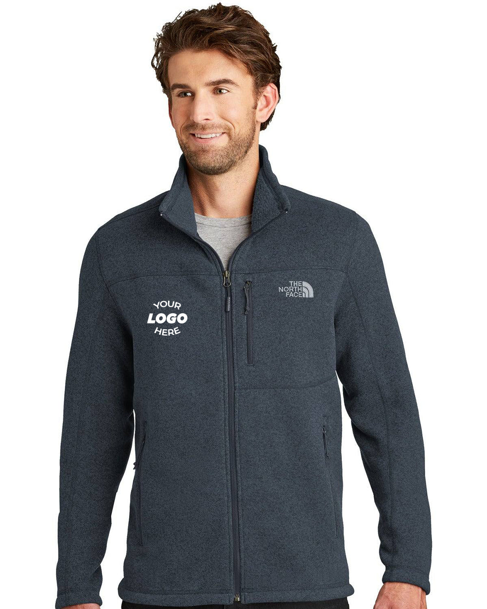 A man wears a dark gray The North Face Sweater Fleece Jacket (NF0A3LH7) with "YOUR LOGO HERE" embroidered on the left chest, standing against a plain white background.