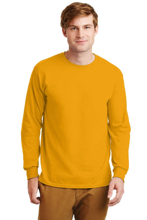A man wears a mustard yellow Gildan 100% US Cotton Long Sleeve T-Shirt 2400 (pack of 36, custom screen printed logo included) and brown pants, standing facing forward against a white background.