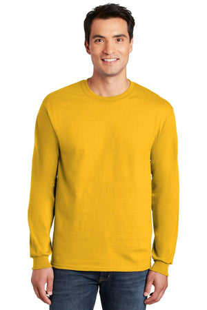 A man stands smiling in a plain background, wearing blue jeans and a yellow Gildan 2400 long sleeve crew neck shirt, made from 100% US cotton, featuring a custom screen printed logo. Available in packs of 36.