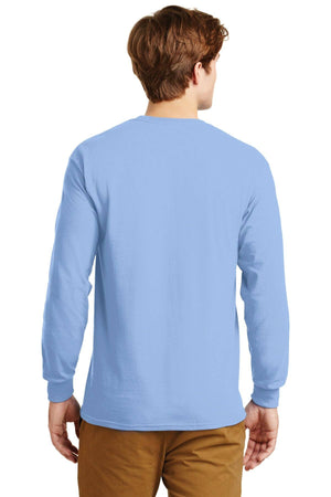 A man stands with his back to the camera wearing brown pants and a light blue Gildan 100% US Cotton Long Sleeve T-Shirt (Pack of 36, style 2400) featuring a custom screen printed logo.