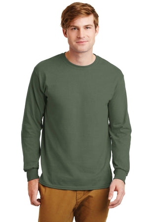 A man faces forward against a white background, wearing a plain olive green Gildan 100% US cotton long sleeve t-shirt (Pack of 36, style 2400) with custom screen printed logo included and tan pants.