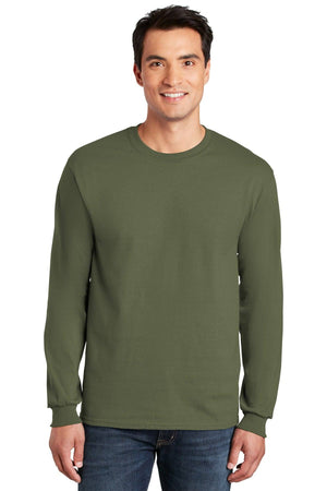 A man smiles facing forward, wearing blue jeans and a plain olive green Gildan 2400 long sleeve T-shirt made from 100% US cotton, with custom screen printed logo included (pack of 36).