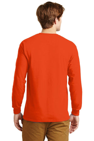 A man stands facing away, wearing a Gildan 100% US cotton long sleeve orange T-shirt (Pack of 36, style 2400) with custom screen printed logo, and tan pants.