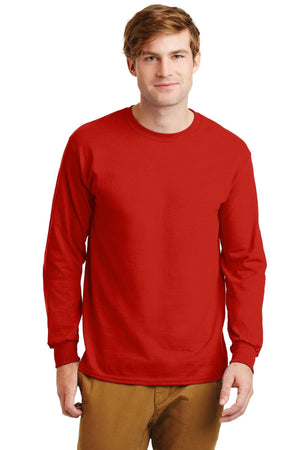 A man stands facing the camera against a white background, wearing tan pants and a plain red Gildan 2400 long sleeve T-shirt made from 100% US cotton, featuring a custom screen printed logo.