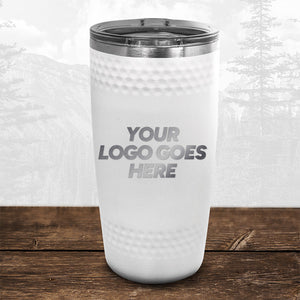 The white golf dimple tumbler from the Golf Course Partner Pack by Kodiak Coolers, featuring "Your Logo Goes Here," is displayed on a wooden surface. This promotional drinkware showcases a grayscale mountainous landscape with trees.
