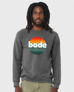 A person wears the designerapp Bode Summer Bootcamp "OG Logo" Unisex Crewneck BC Fleece Raglan Sweatshirt 3901, featuring a sunset graphic and text on soft Airlume cotton, printed with Direct to Garment technology.