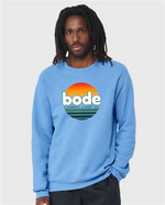 A man wearing a light blue designerapp Bode Summer Bootcamp "OG Logo" unisex crewneck BC fleece raglan sweatshirt 3901 with a sunset graphic.