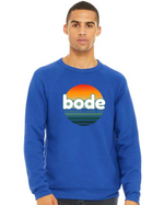 A person wears the designerapp Bode Summer Bootcamp "OG Logo" unisex crewneck BC fleece raglan sweatshirt 3901, crafted from soft, pre-shrunk Airlume cotton and featuring a retro sunset-striped graphic.