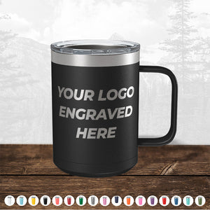 A black Kodiak Coolers insulated tumbler with a clear lid and handle, featuring a placeholder text "your custom logo here" on a wood surface, with a faded forest background.