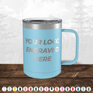 A light blue insulated tumbler with a silver rim and handle, custom printed with your logo, displayed on a wooden surface against a blurred forest background. TODAY ONLY - Hump Day Sale - Your Logo Engraved on Drinkware - Single Side Engraving Included in Price - Slider Lids Included by Kodiak Coolers.