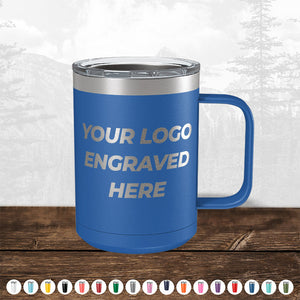 Blue insulated tumbler with a handle on a wooden surface, featuring the text "your logo engraved here" in a forest background—perfect as a promotional gift from Kodiak Coolers' TODAY ONLY - Custom Logo Drinkware Sale - Your Logo Laser Engraved INCLUDED in Price - No Hidden Fee's.