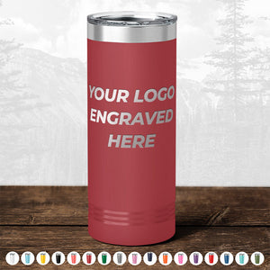A red insulated tumbler with "your logo engraved here" text, displayed in front of a blurry forest background. Various color options are shown below for these Kodiak Coolers promotional gift mugs.