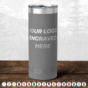A Kodiak Coolers stainless steel insulated tumbler with the text "TODAY ONLY - Custom Logo Drinkware Sale - Your Logo Laser Engraved INCLUDED in Price - No Hidden Fee's" displayed on a wooden surface, ideal as a promotional gift, with a blurred forest background.