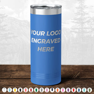 A blue insulated tumbler with "your custom logo engraved here" text, displayed on a wooden surface against a blurred forest background. Various color options are shown below from Kodiak Coolers.