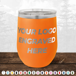 An orange stainless steel tumbler from Kodiak Coolers, featuring "YOUR LOGO ENGRAVED HERE" text on the front side. The background showcases a serene nature landscape with trees and mountains, making it an ideal promotional gift. Below, you can see a selection of 12 different colored custom mugs available in our HUGE LABOR DAY SALE - ENDS TODAY!